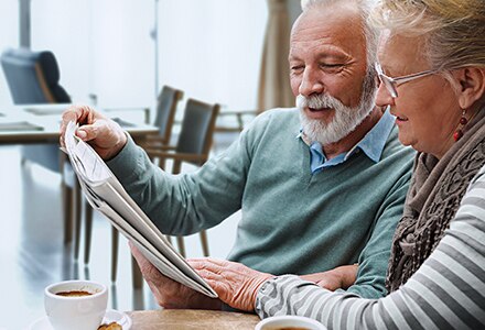 Man & Woman Reading Newspaper Enjoying Coffee in Senior Living Facility