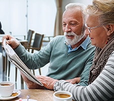 Man & Woman Reading Newspaper Enjoying Coffee in Senior Living Facility