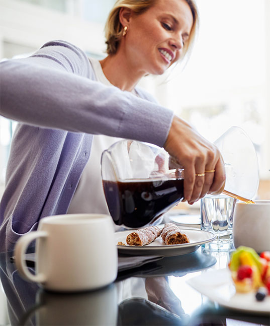 Woman Pouring Cup of Hot Coffee at Breakfast